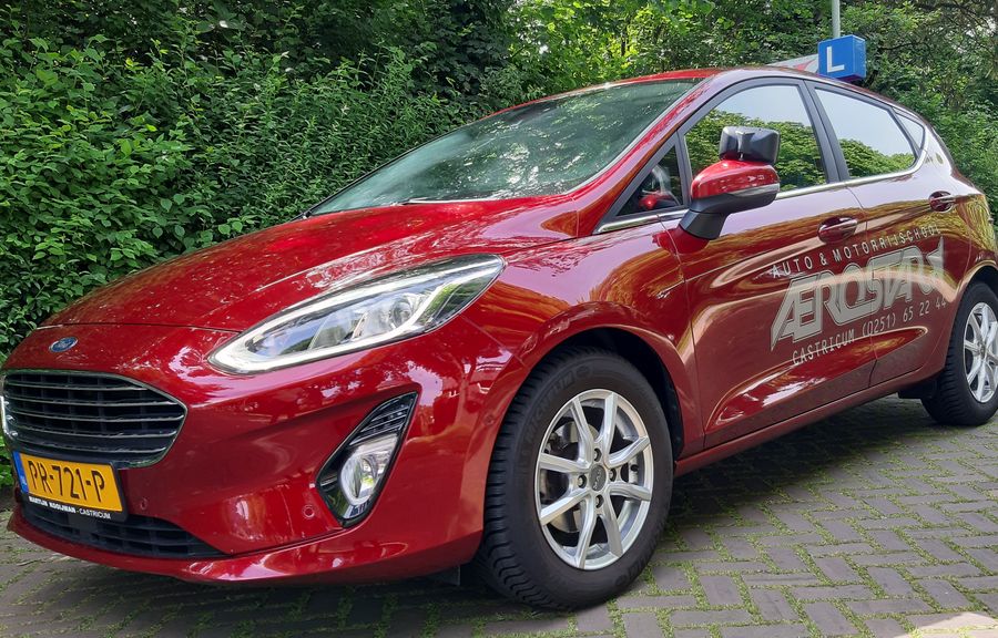 De rode Ford Fiesta lesauto van Aerostar met een blauw L-bord op het dak