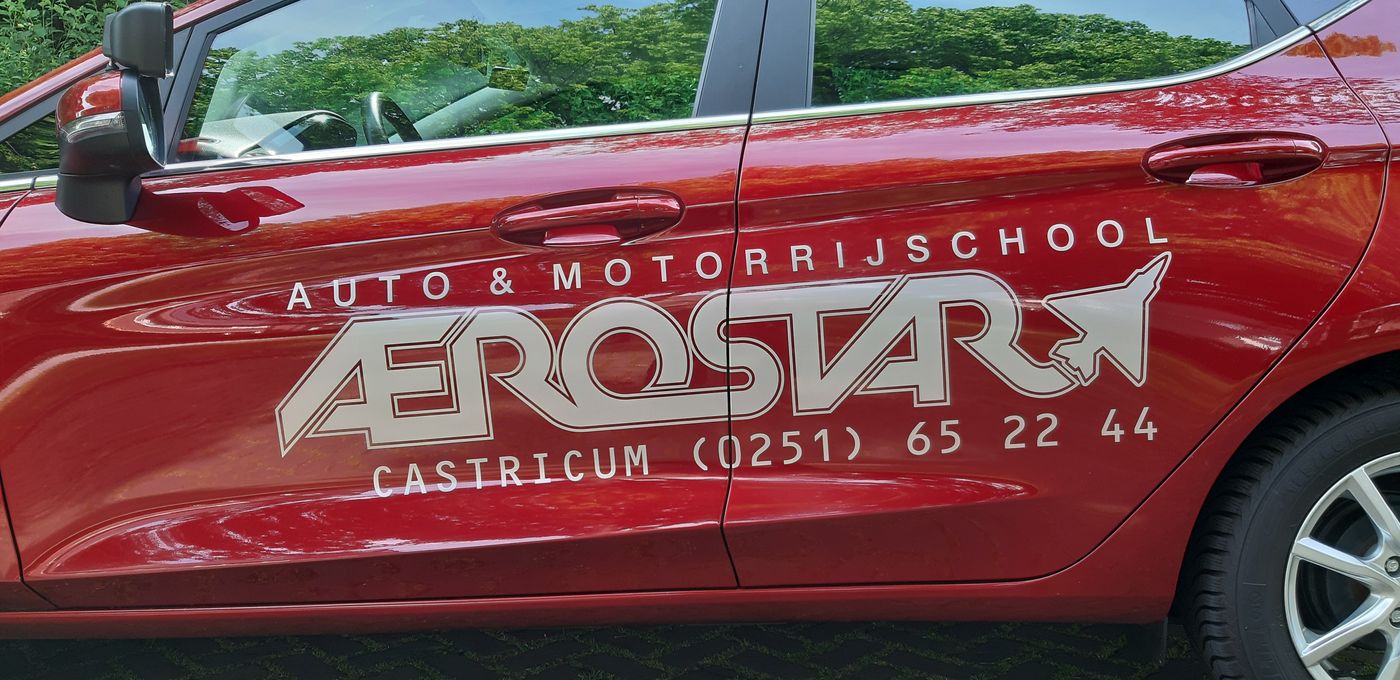 De rode lesauto van Aerostar met de belettering Auto en Motorrijschool Aerostar Castricum